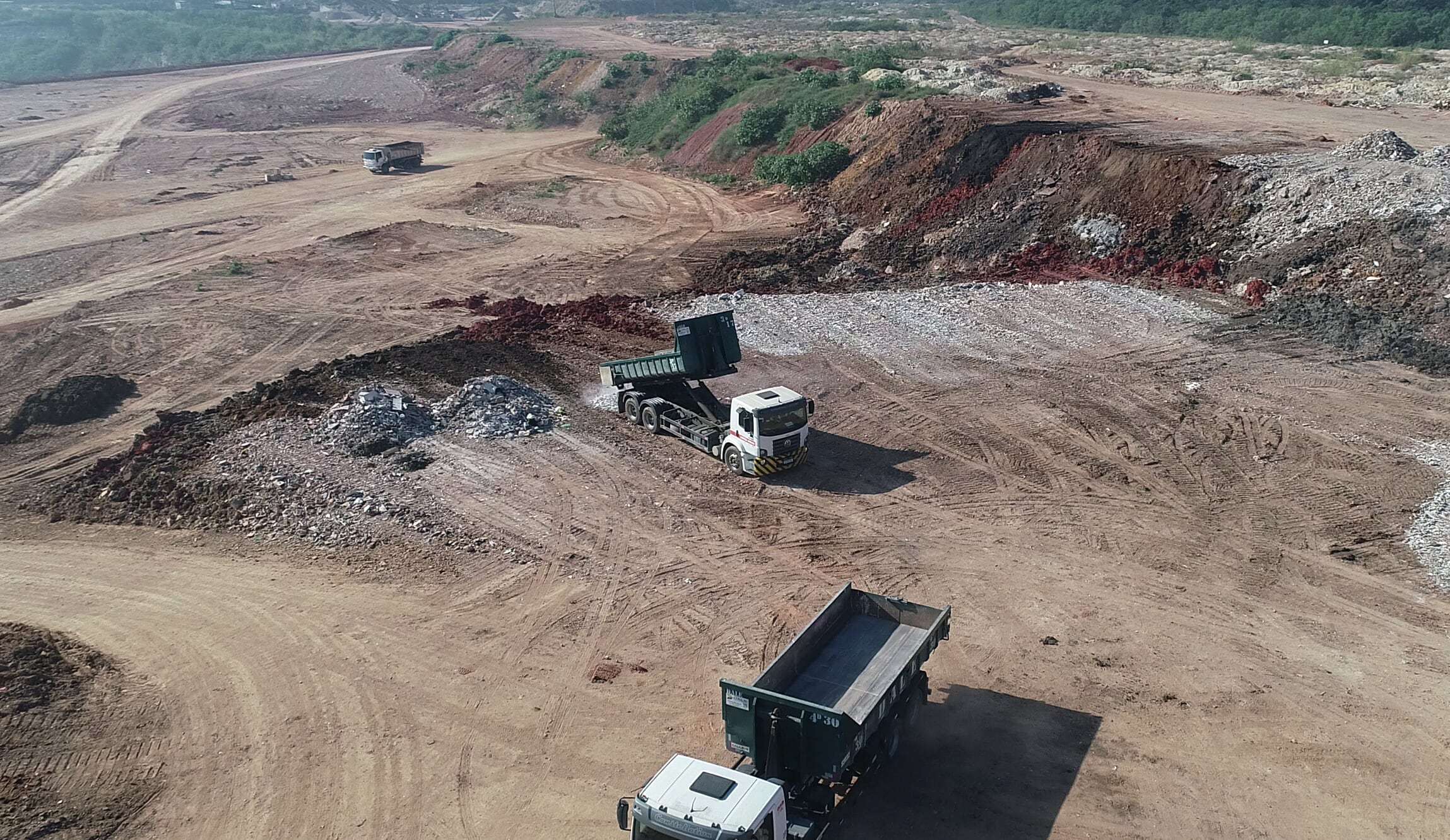 Dois caminhões basculantes na frente de descarte do aterro, vistos de cima